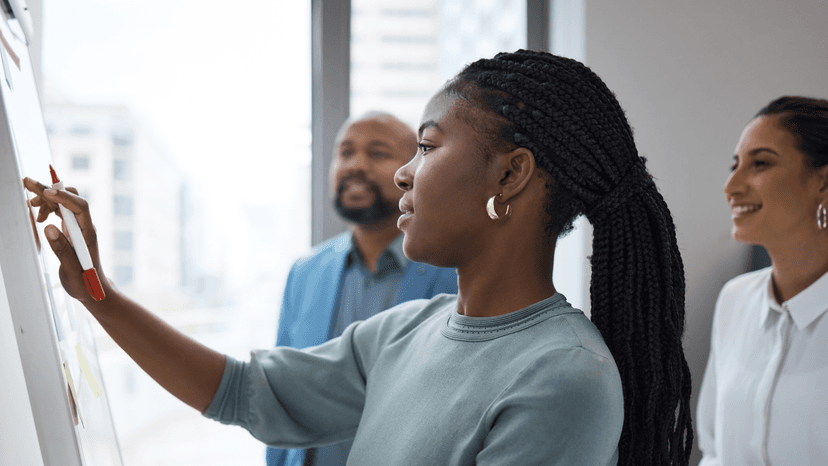 Woman working on a whiteboard in front of two people